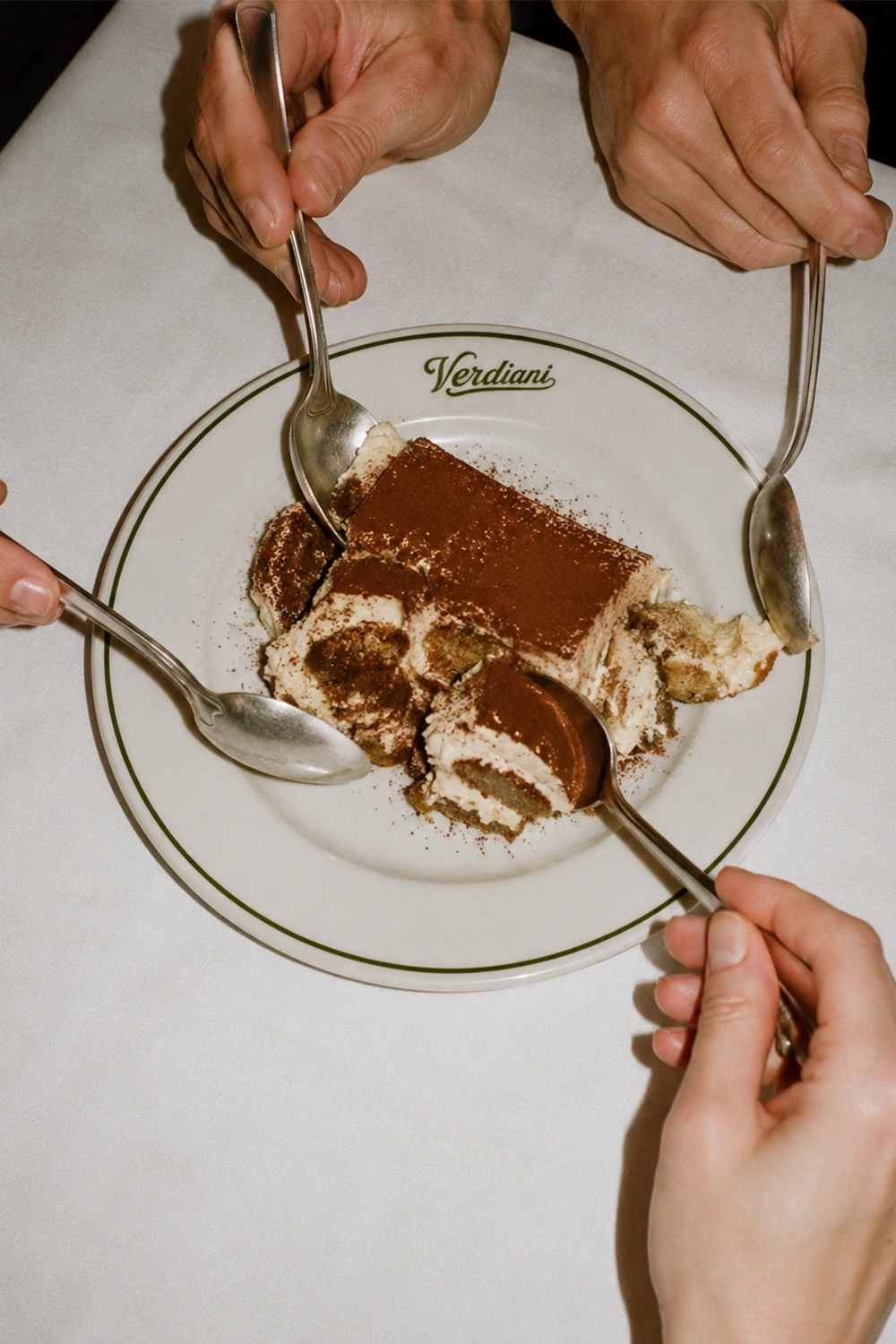 Four spoons sharing a plate of tiramisu